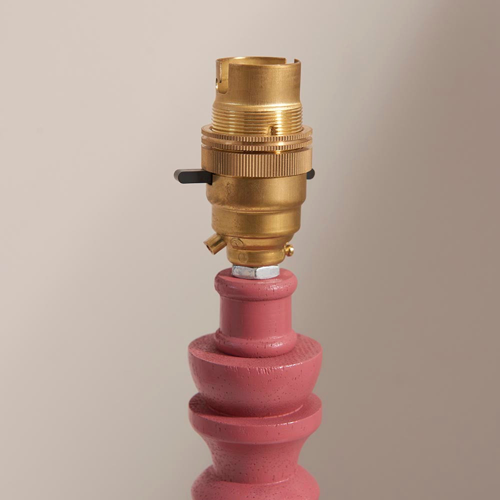 Endon Aldworth table lamp close-up showing the brass B22 switched lampholder above a pink satin painted turned wood spindle, on a neutral background.