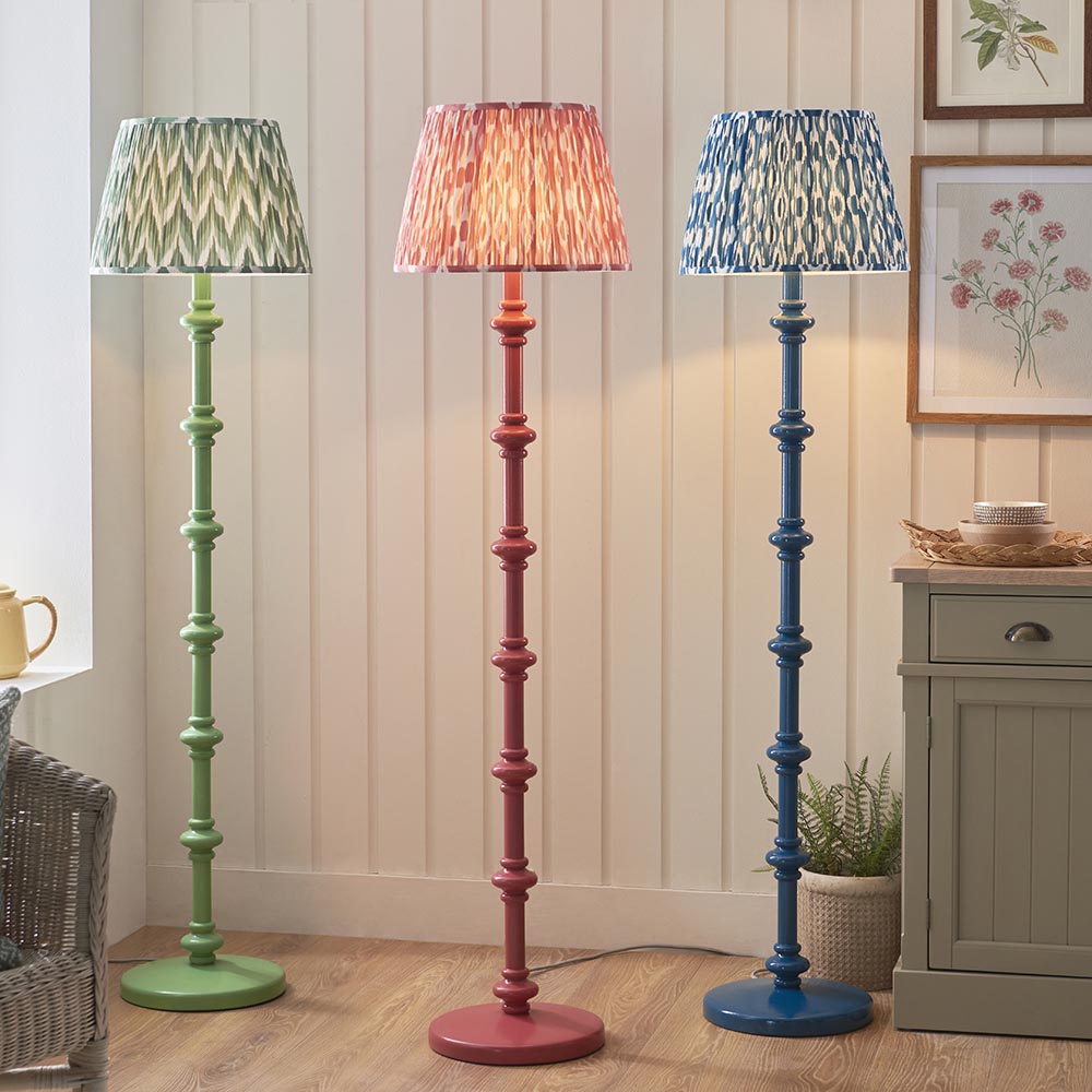Endon Bevbury turned spindle floor lamps in green, pink and blue satin finishes with patterned fabric shades, displayed in a living room beside a cabinet.