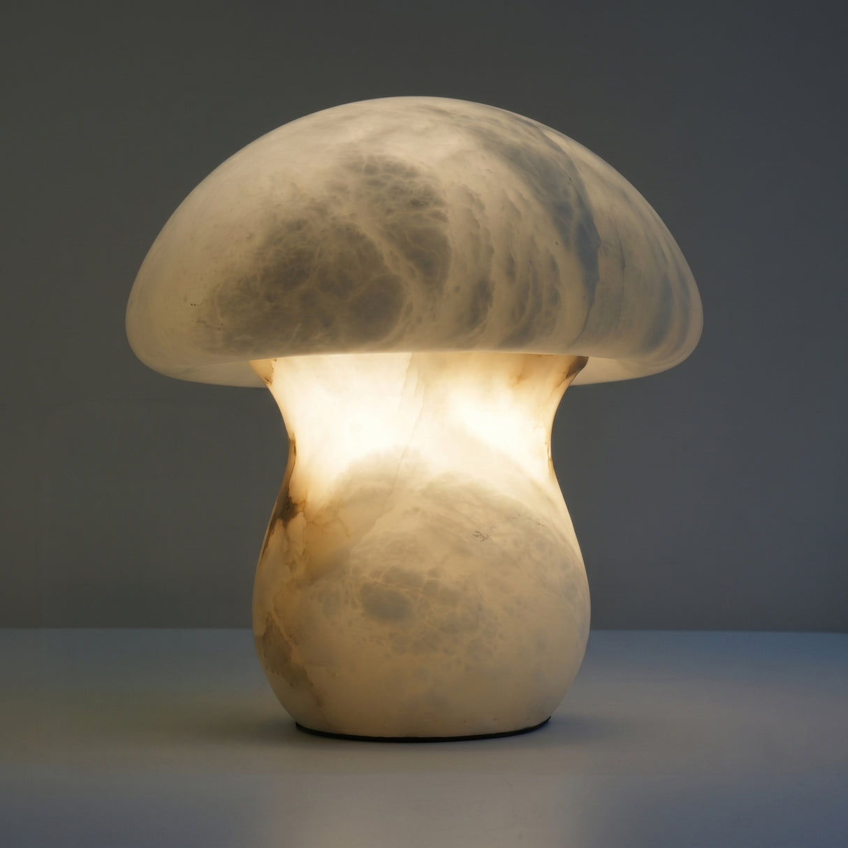 Morfia Mushroom Alabaster Table Lamp in soft white, carved from solid alabaster with a domed cap and stem glowing warmly from within, shown against a plain grey background.