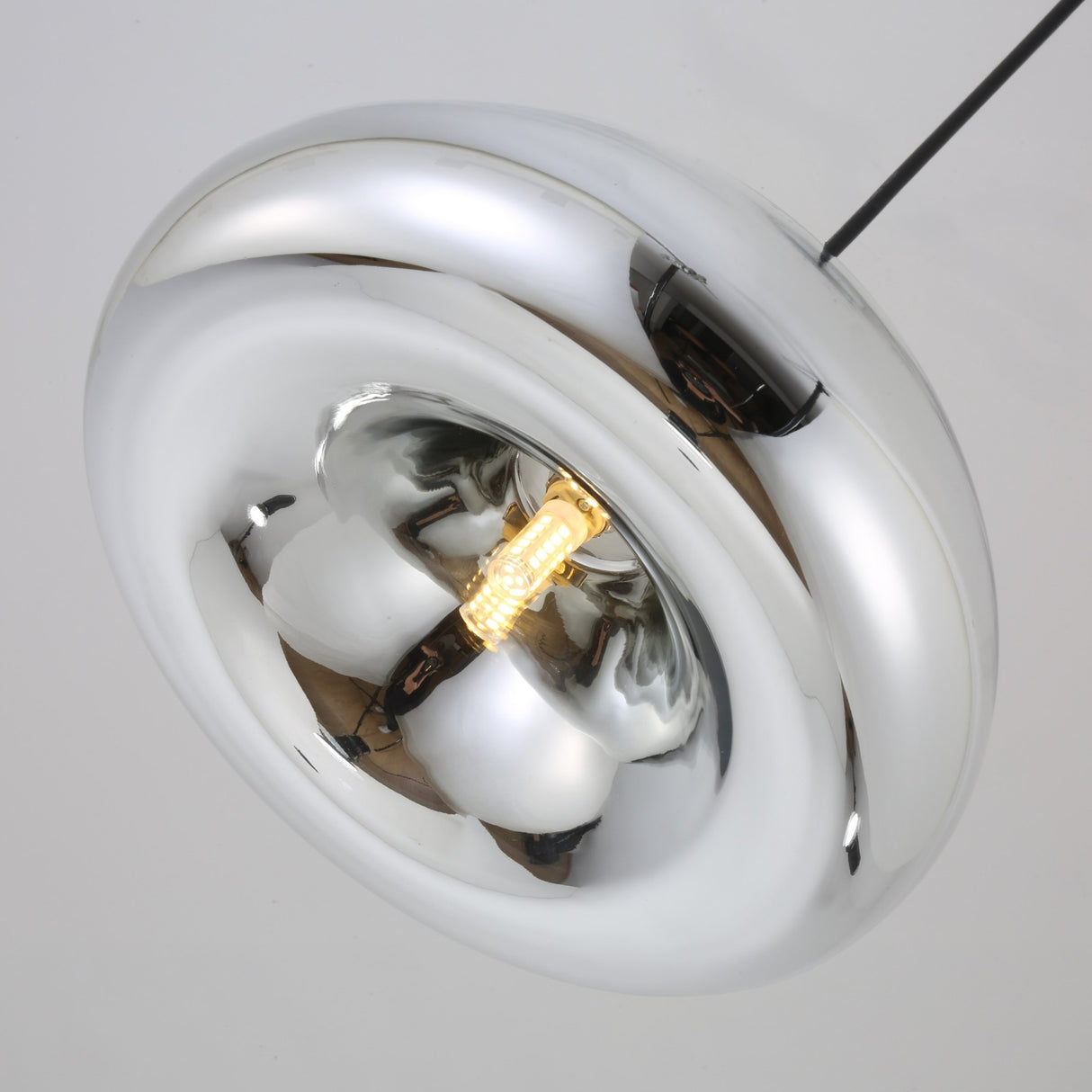 The Gulf Mini Glass Pendant Light - Silver features a modern circular metallic design with a reflective chrome finish, a visible glowing bulb, and hangs from a black cord against a light background.