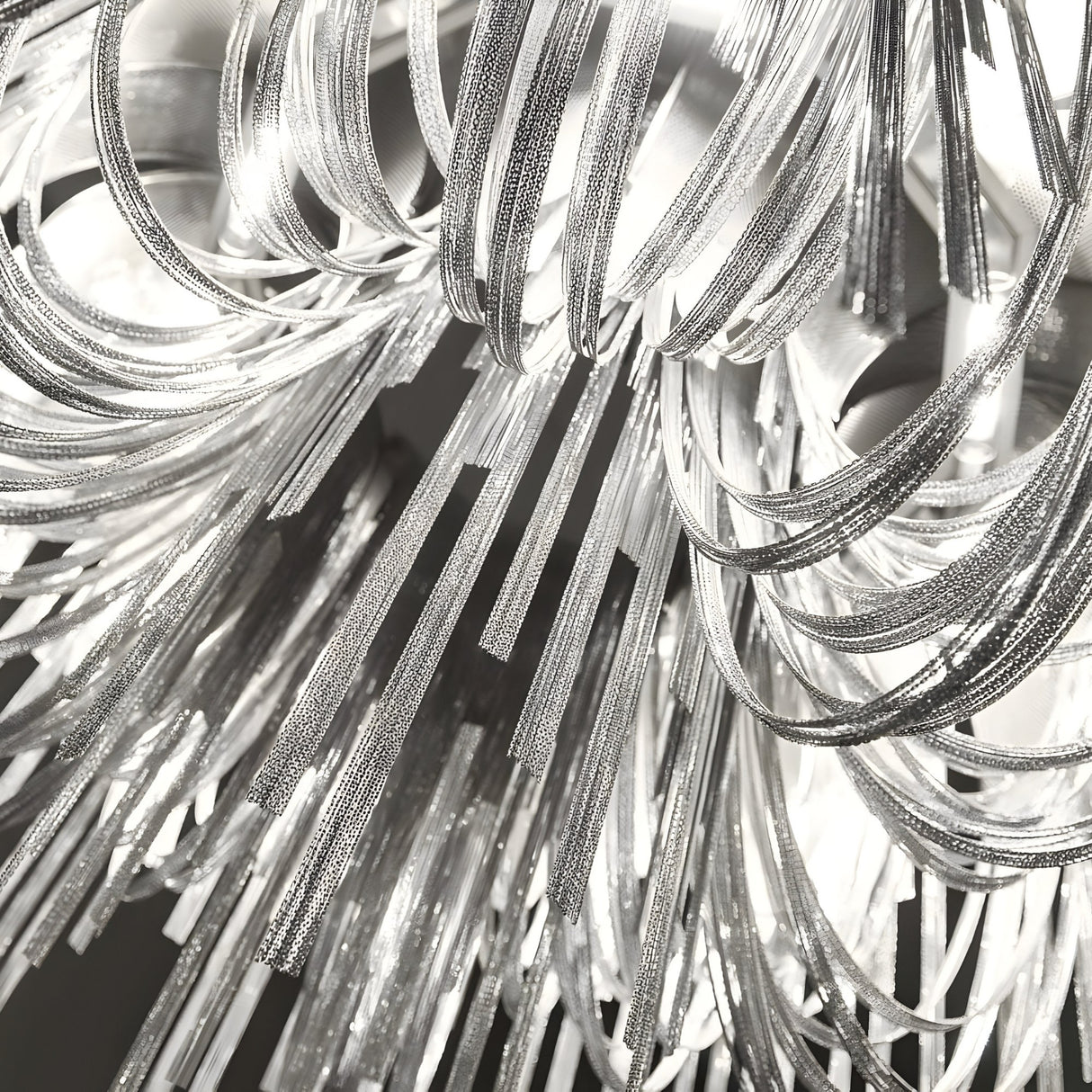 Close-up of the Symphonia 10 Light Metal Chain Veil Small Chandelier in nickel, featuring silver reflective strips in curved and straight lines. Its bright LED lights shine through, casting intricate, abstract patterns.