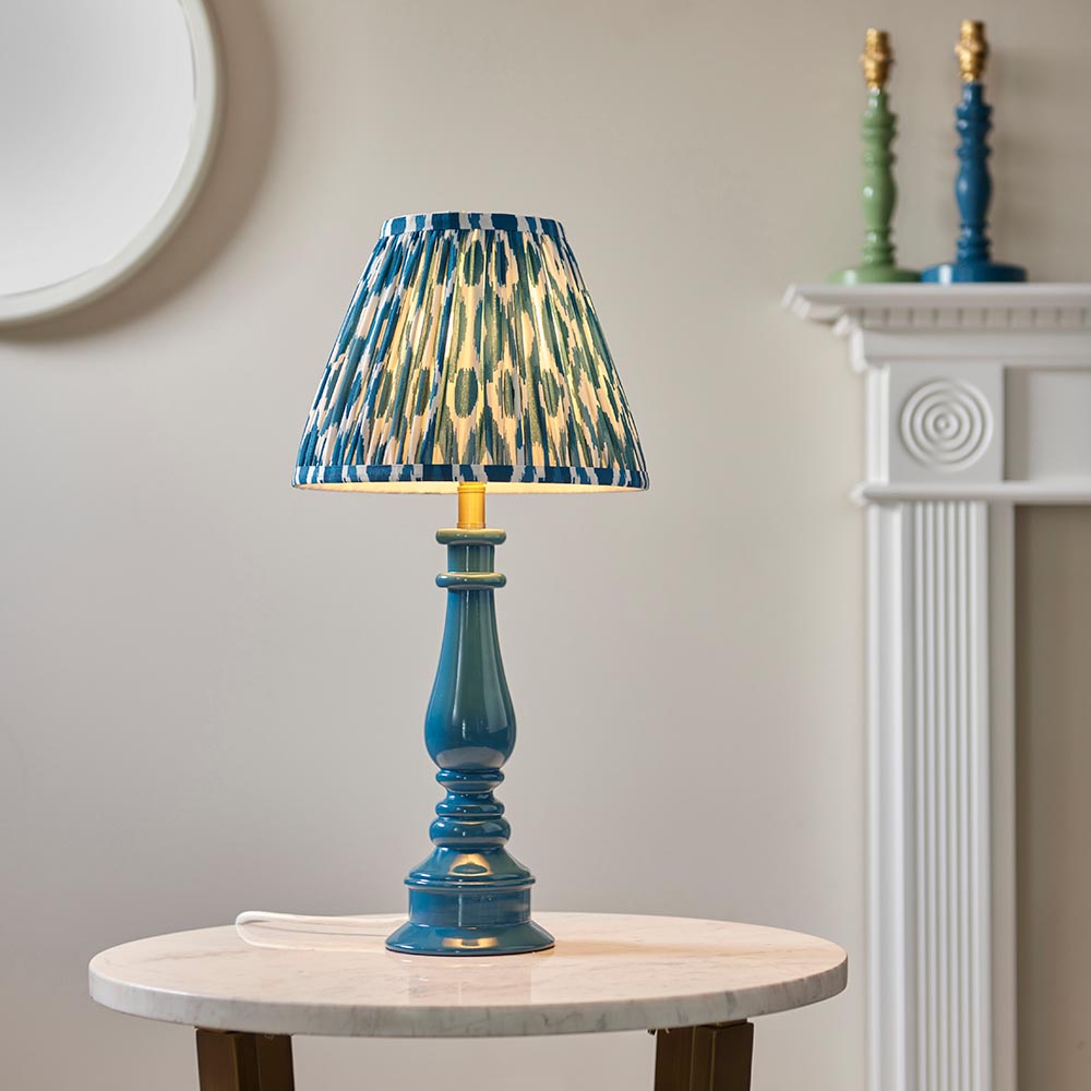 Endon Carlworth table lamp with gloss blue turned spindle base, brass holder and pleated blue patterned shade, on a marble side table by a fireplace.