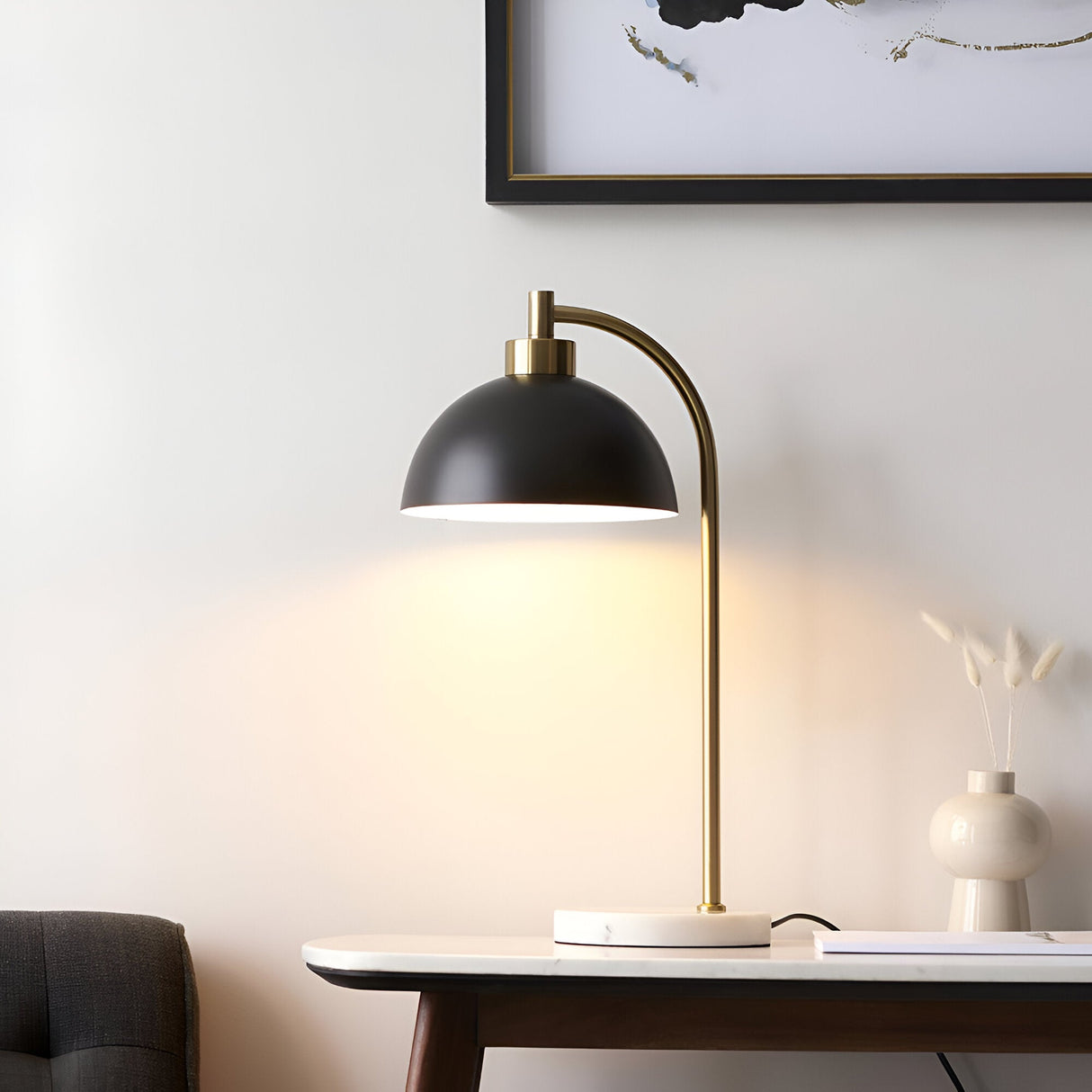 Endon Ashmont table lamp with matt black dome shade, arched antique brass stem and white marble base, on a console beneath framed wall art.