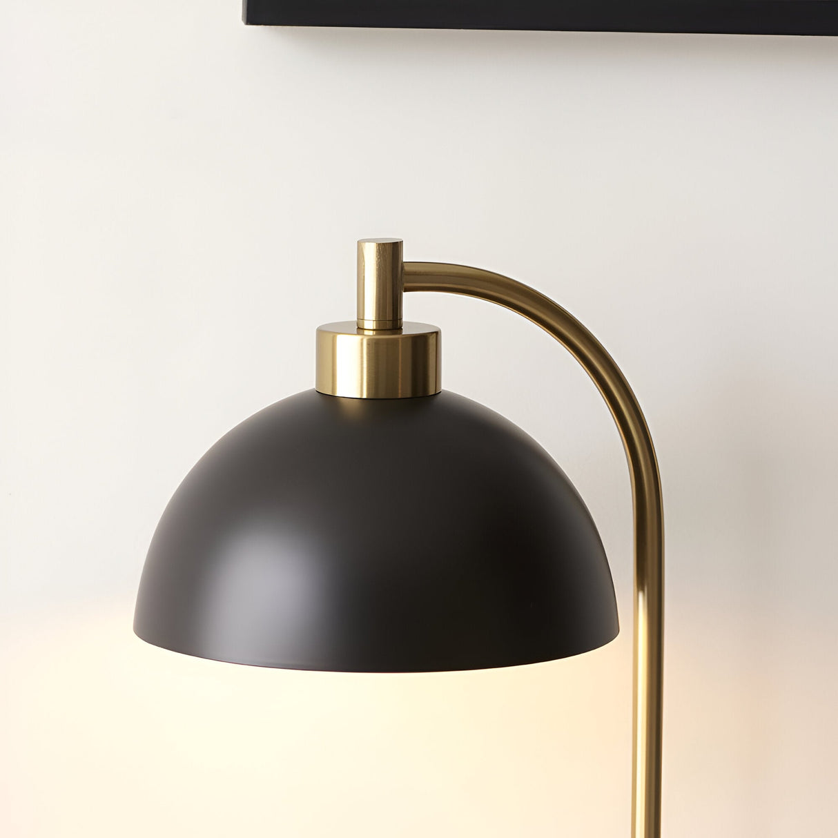 Endon Ashmont table lamp close-up showing matt black dome shade and curved antique brass stem against a pale wall.