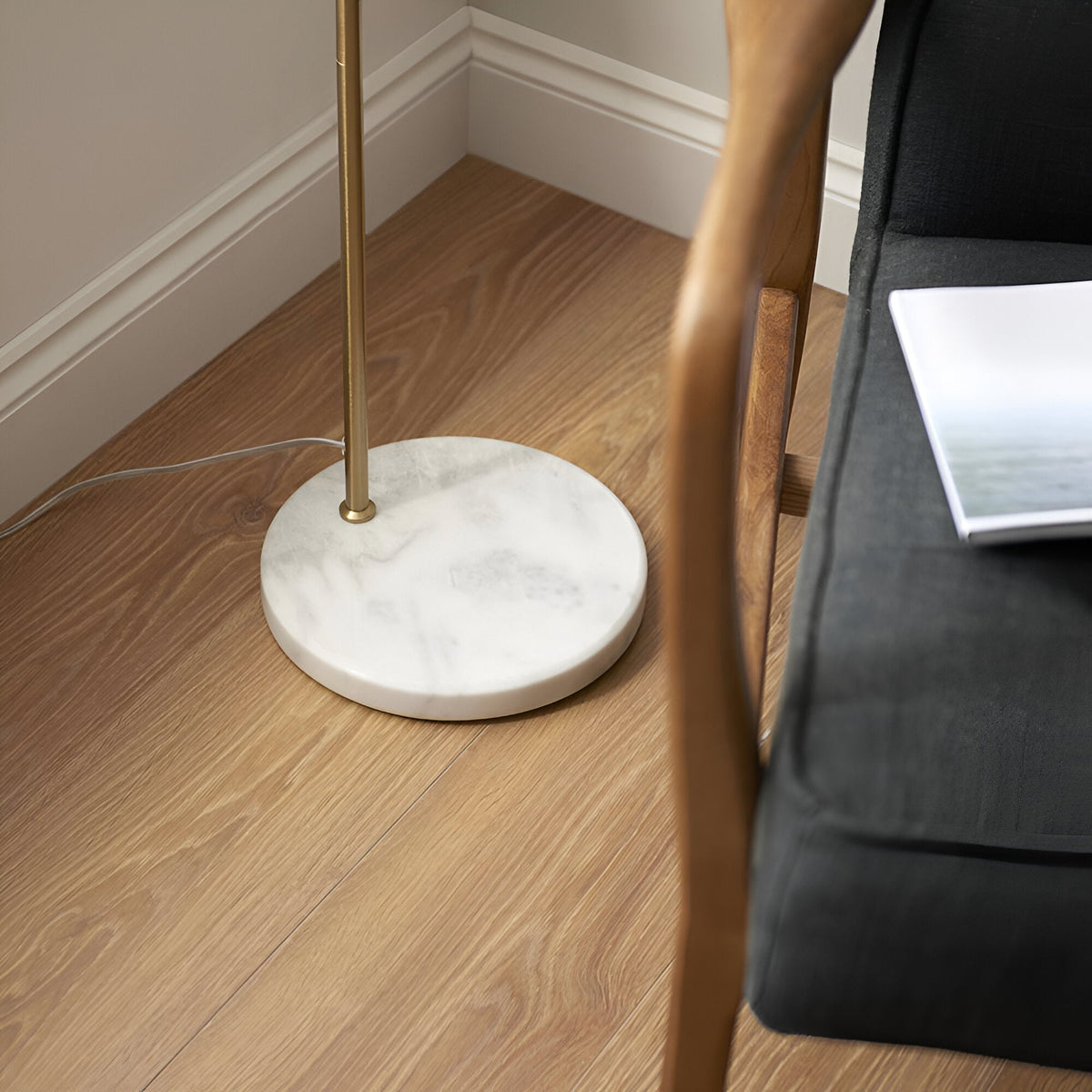 Endon Ashmont floor lamp base in a living room corner, showing the white and grey marble disc and antique brass stem beside a wooden chair.
