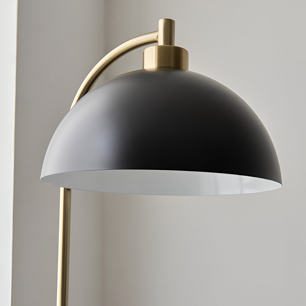Close-up of the Endon Ashmont Floor Lamp showing its matt black dome shade and antique brass arched stem against a light neutral background.