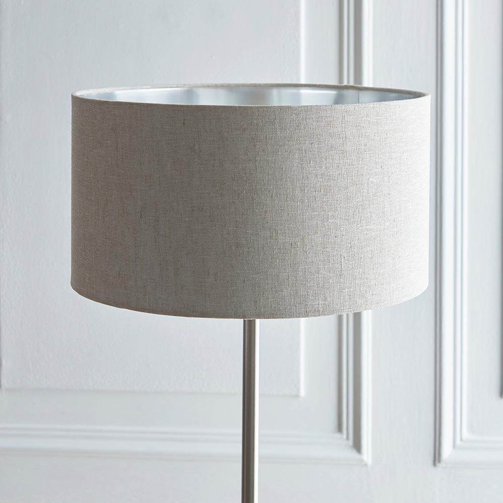Endon Brenley floor lamp with a natural linen drum shade, reflective metallic inner and slim chrome stem, set against a white panelled wall.