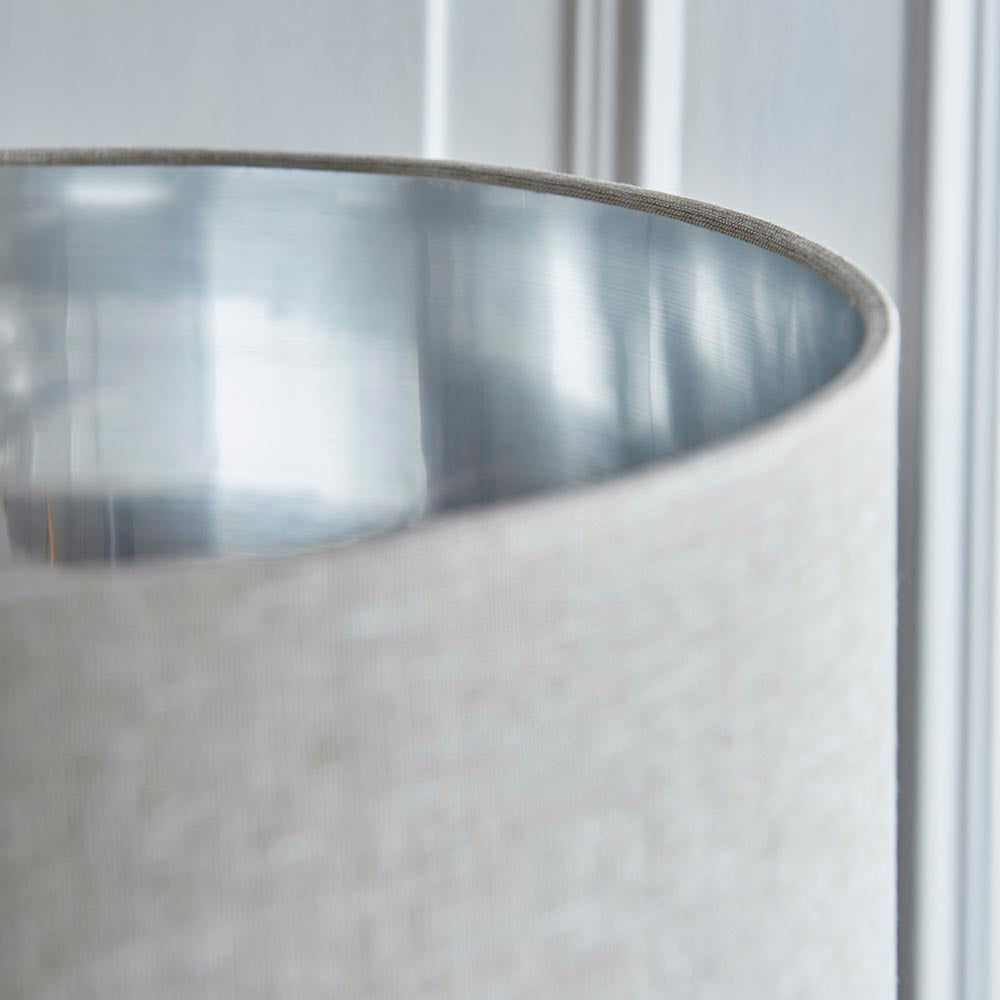 Close-up of the Endon Brenley floor lamp shade showing a natural linen exterior and brushed chrome metallic inner lining against a pale panelled wall.