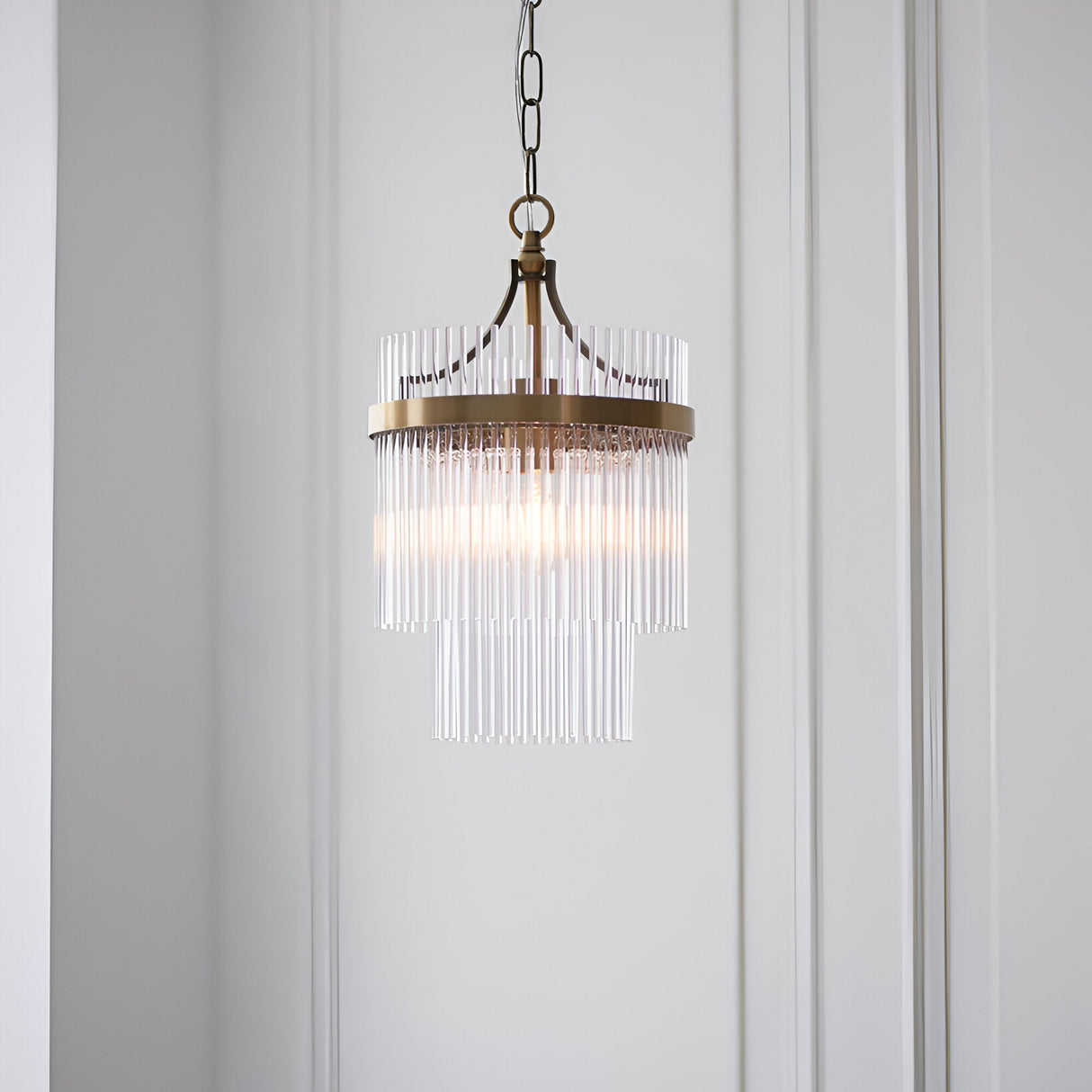 Endon Beaumont two-tier pendant in antique brass with clear glass rod fringe and chain suspension, hung against a white panelled wall.