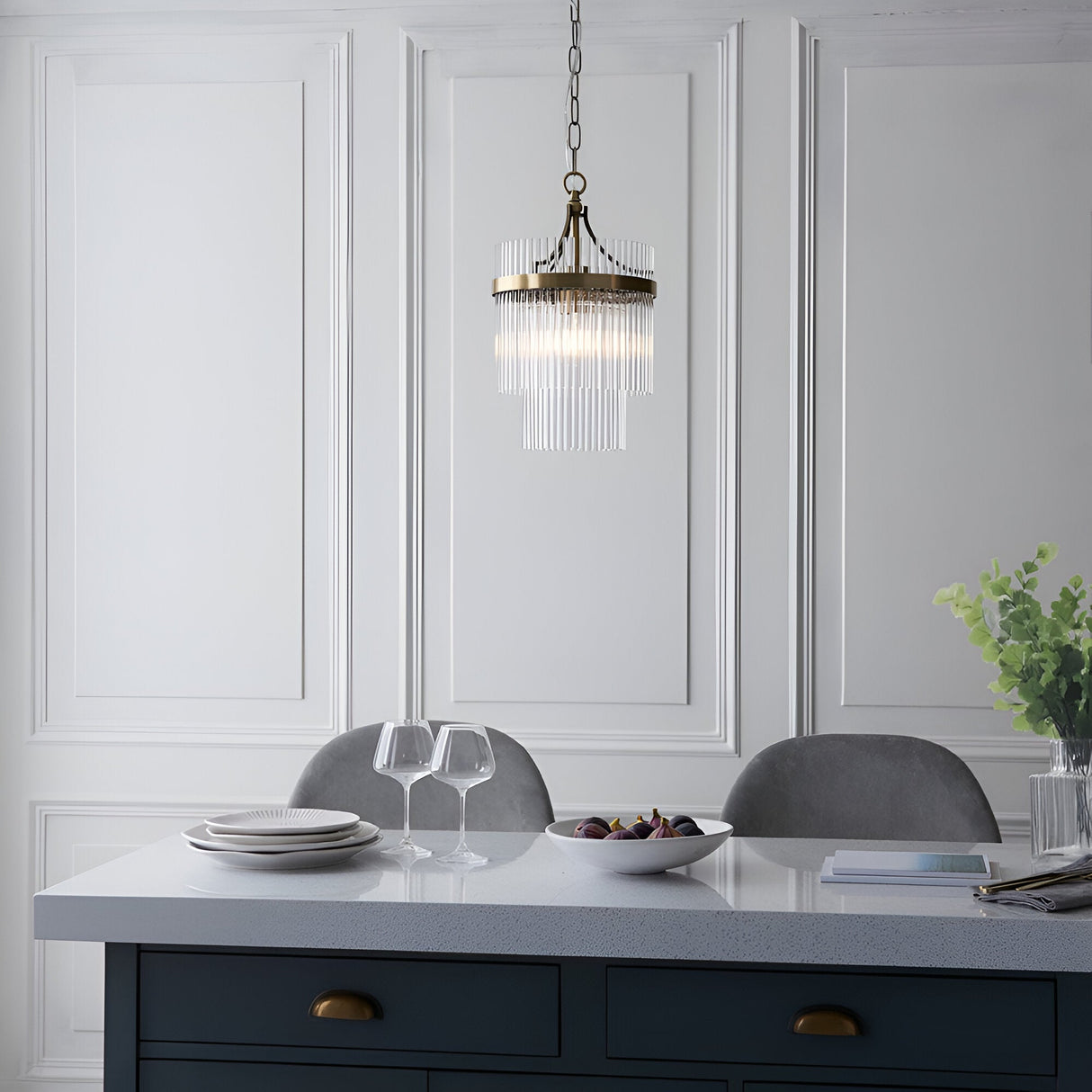 Endon Beaumont pendant in antique brass with tiered clear glass rods, hung from a chain above a kitchen island with grey chairs and panelled wall.