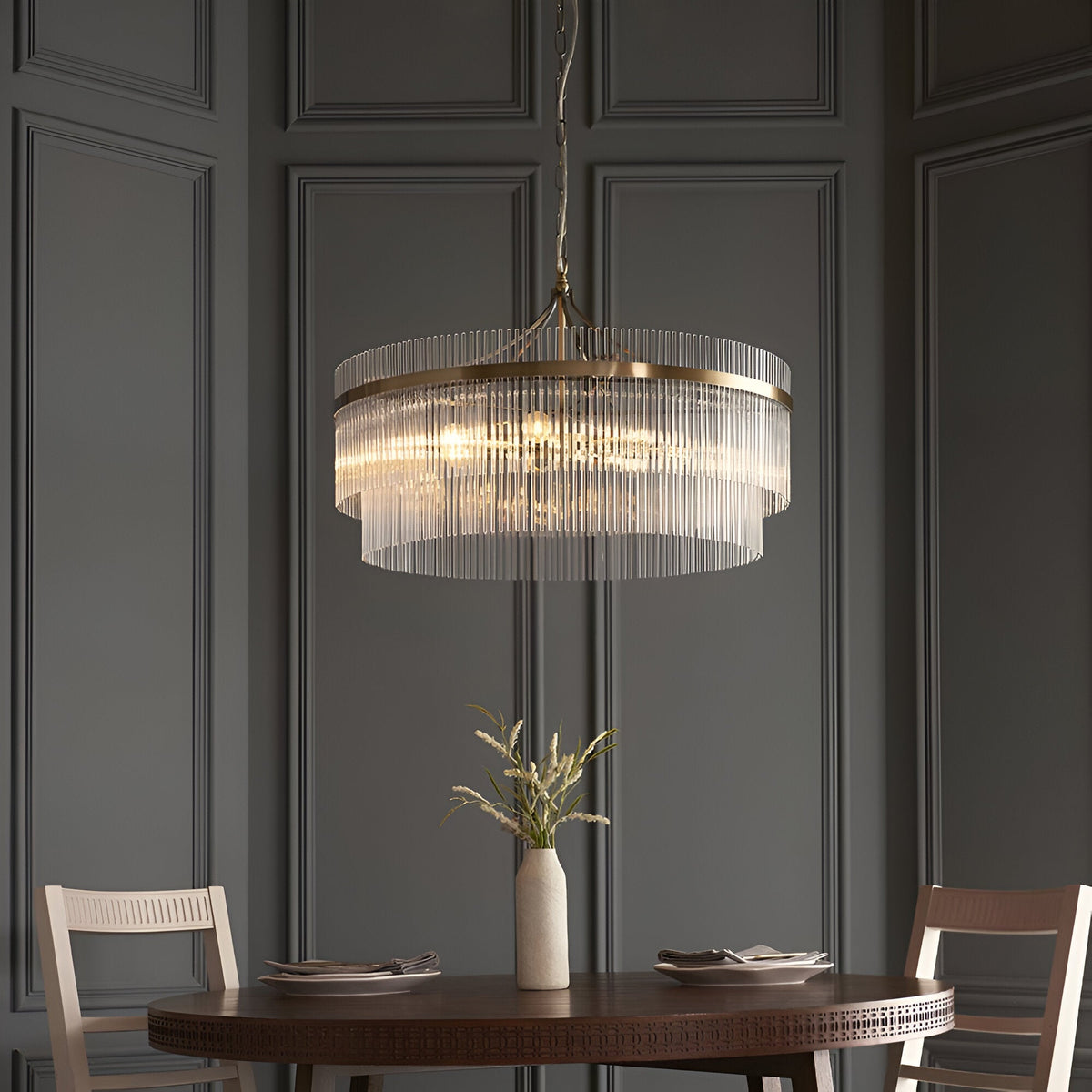 Endon Beaumont 7 light pendant in antique brass with tiered clear glass rods, hung above a dining table against grey panelled walls.