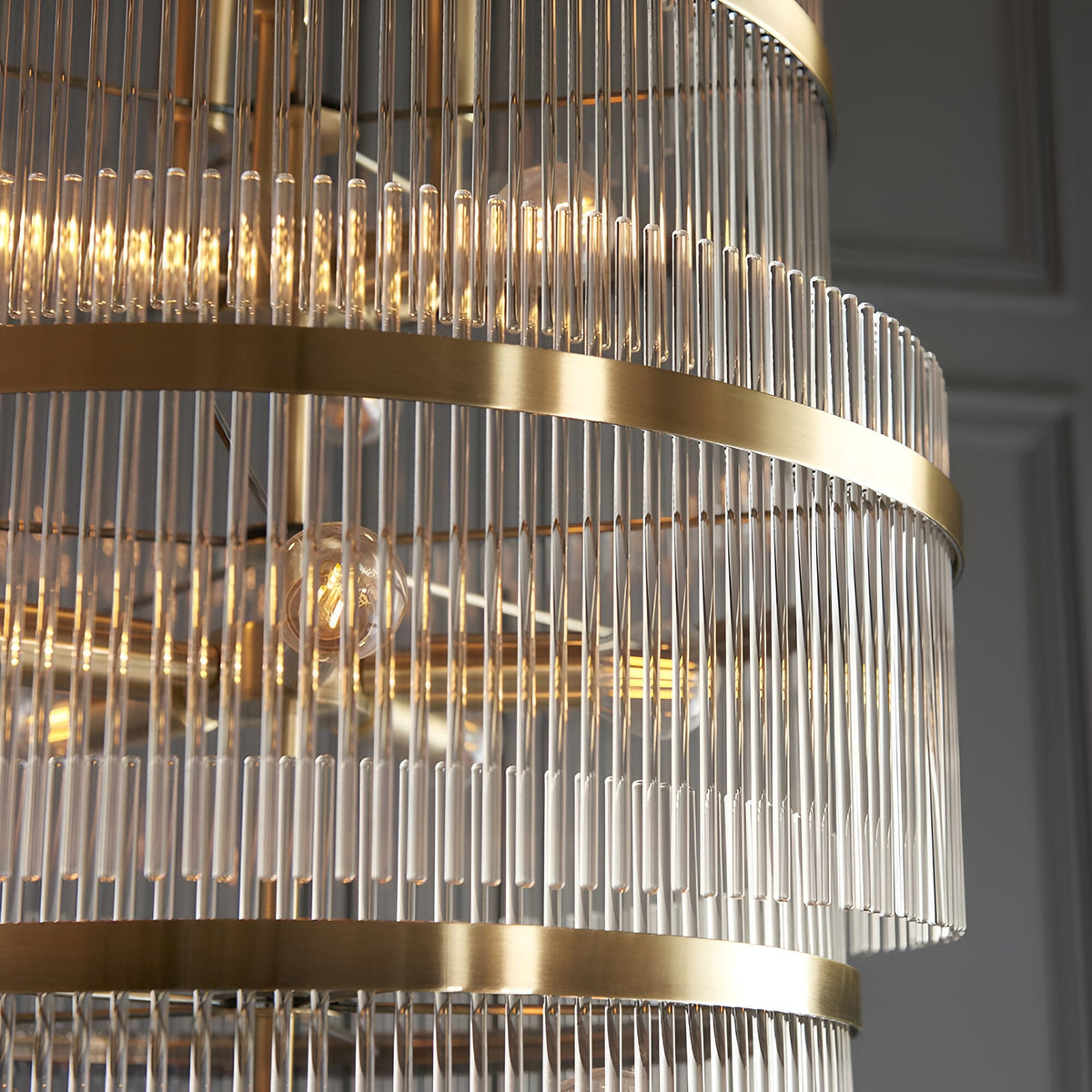 Close-up of Endon Beaumont 21 light chandelier in antique brass, showing tiered bands of clear glass rods and lit E14 bulbs within.