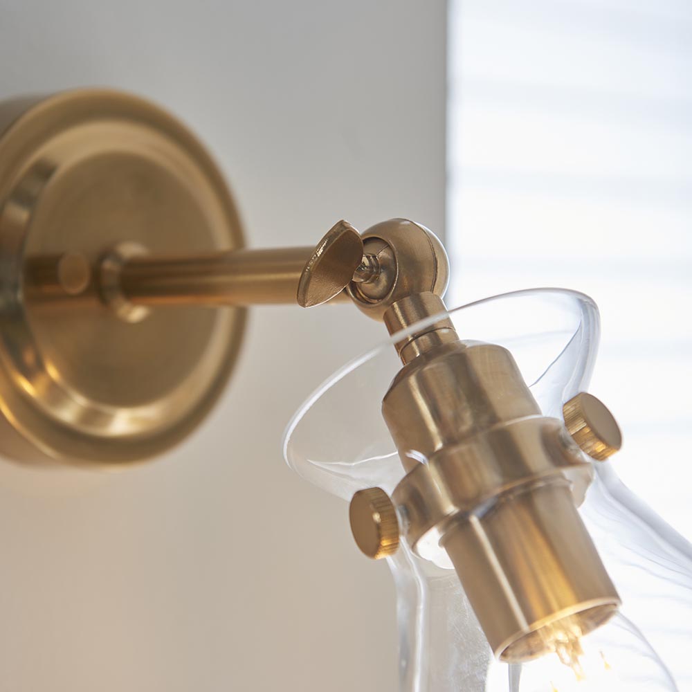 Close-up of the Endon Brenbury wall light showing its brushed antique brass adjustable knuckle, round backplate and clear glass shade.