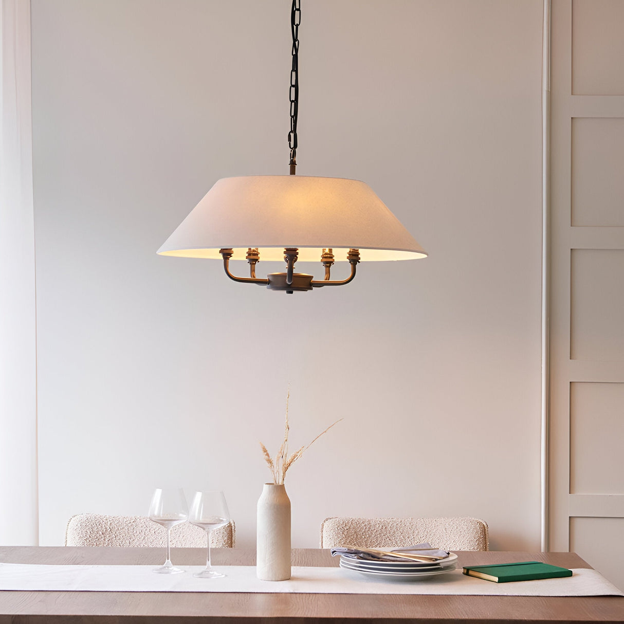 Endon Caldmere 5 light pendant with wide natural linen shade and black chain suspension, hung above a dining table with wine glasses and vase.