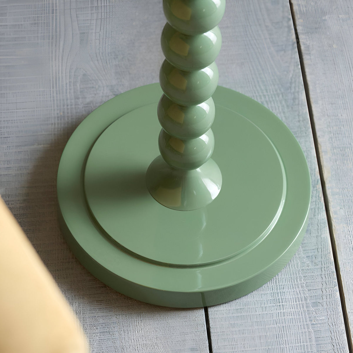 Close-up of the Brenleigh Floor Lamp's base in green, showing stacked metal spheres and a round tiered plinth on a wooden floor.