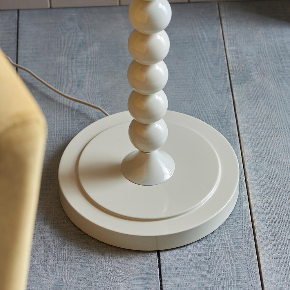 Endon Brenleigh floor lamp base in glossy white with stacked metal spheres on a round base, shown on grey plank flooring beside a yellow chair.
