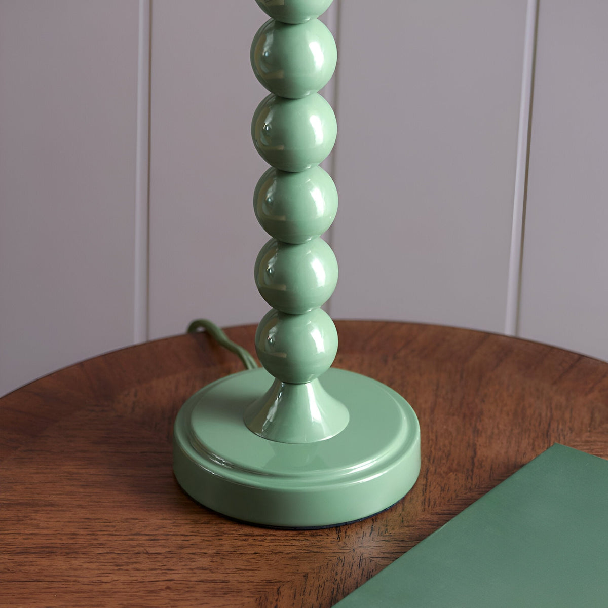 Endon Brenleigh table lamp base in glossy Cotswold Green, with stacked metal spheres and a round base, shown on a wooden side table.