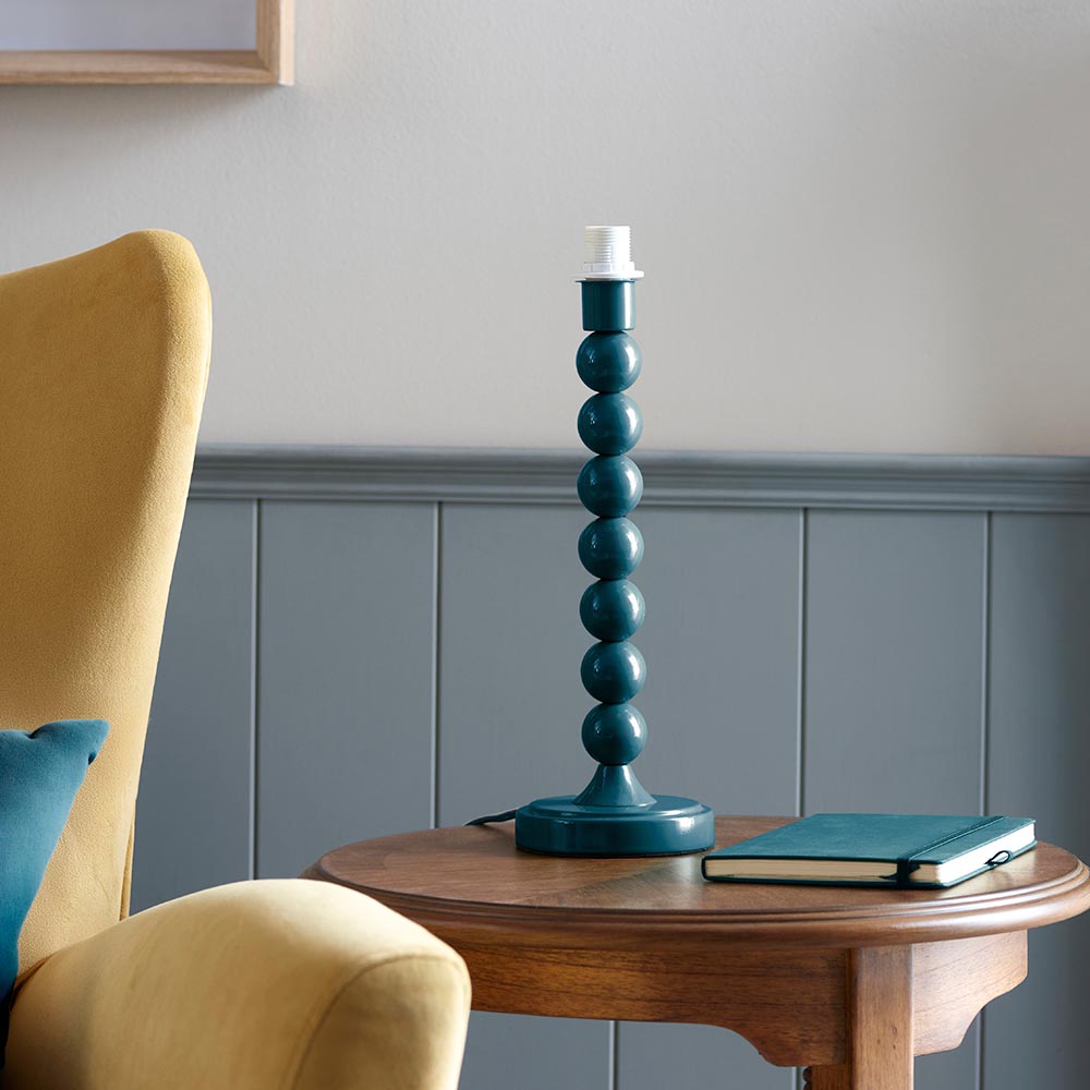 Brenleigh Table Lamp base in blue, stacked glossy metal spheres on a round foot, shown shadeless on a side table beside a notebook.