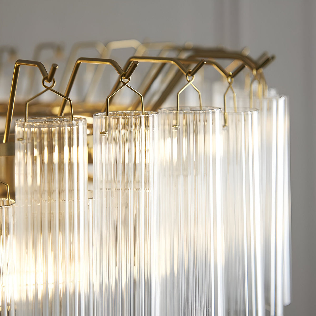 Close-up of Endon Cranshaw 12 light tiered pendant showing ribbed clear glass cylinders suspended from satin brass hooks on the frame.