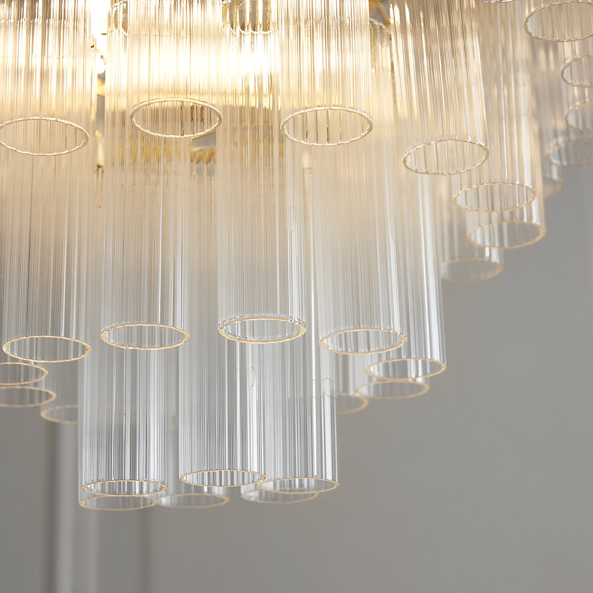 Close-up of the Endon Cranshaw 12 light tiered pendant showing ribbed clear glass cylinders layered on satin brass metalwork with warm glowing lamps above.