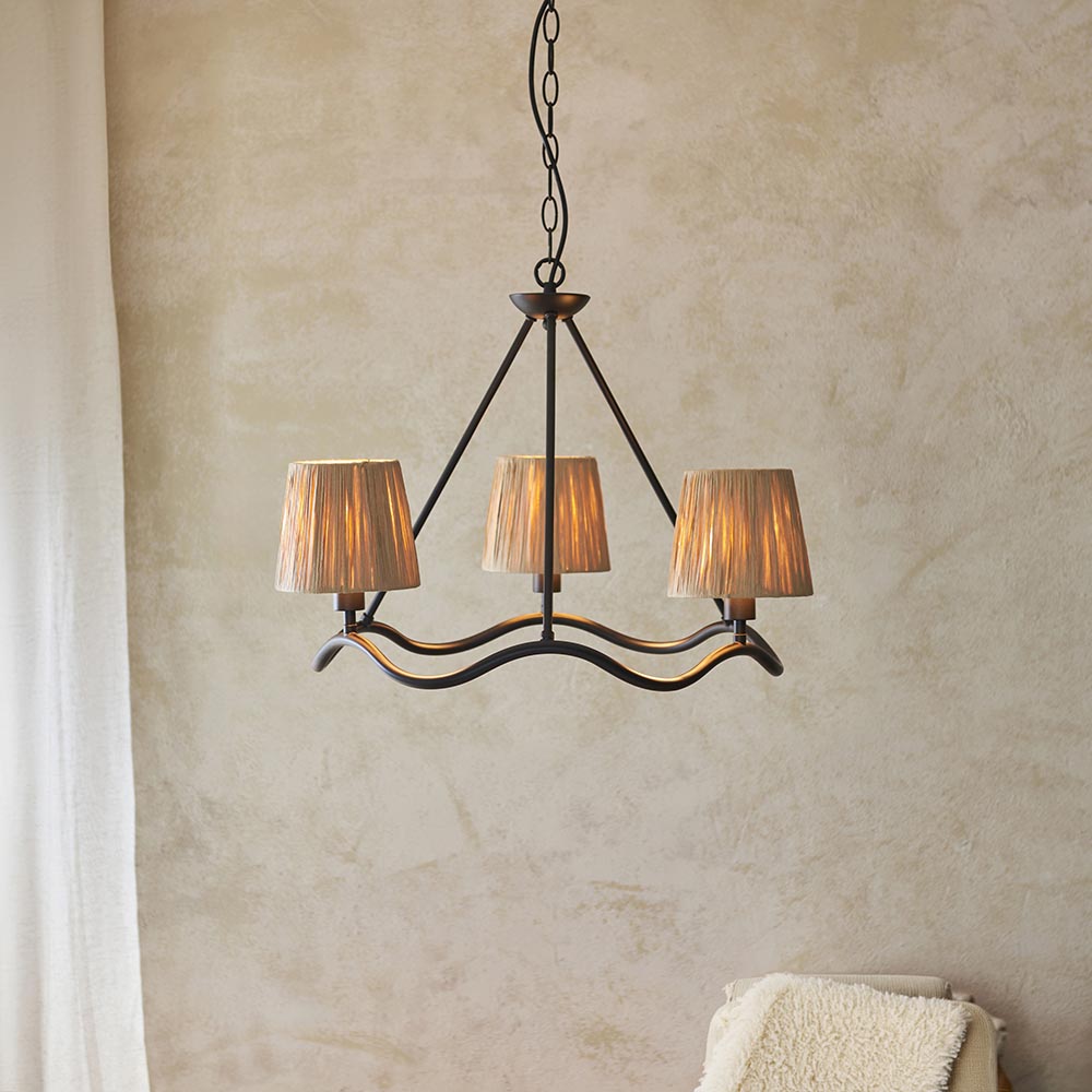 Endon Danemont 3 Light Pendant in black with a wave-shaped hoop and three hand-wrapped raffia tapered shades, hung from a chain against a plaster wall.