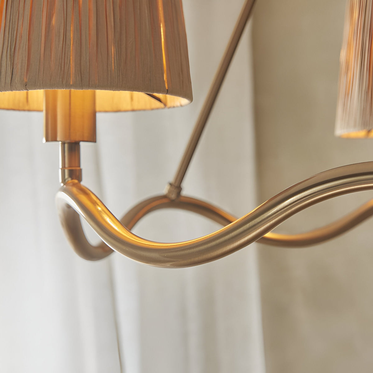 Close-up of the Danemont 3 Light Pendant in brass, showing the wave-shaped metal hoop and a hand-wrapped raffia shade against a soft neutral background.