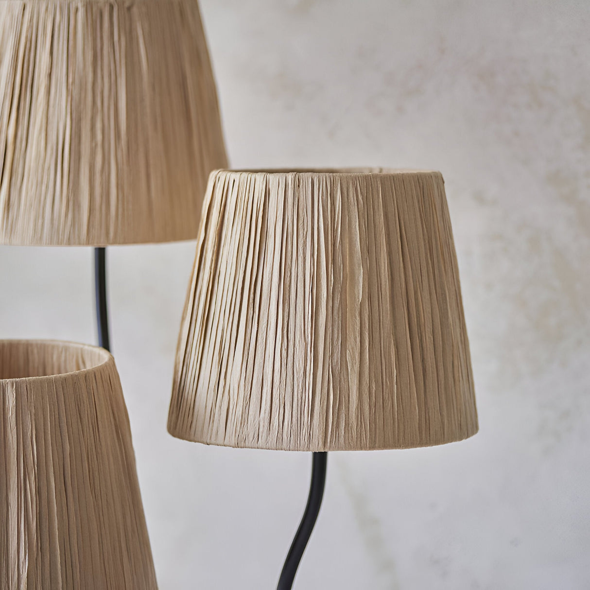 Close-up of Endon Danemont 3 Light Floor Lamp in black, showing three tapered hand-wrapped raffia shades on slender matt black arms against a pale wall.