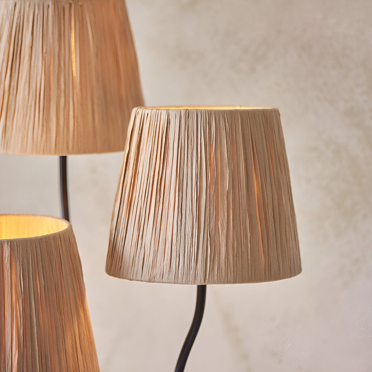 Close-up of the Endon Danemont 3 light floor lamp showing three tapered hand-wrapped raffia shades on matt black arms against a pale wall.