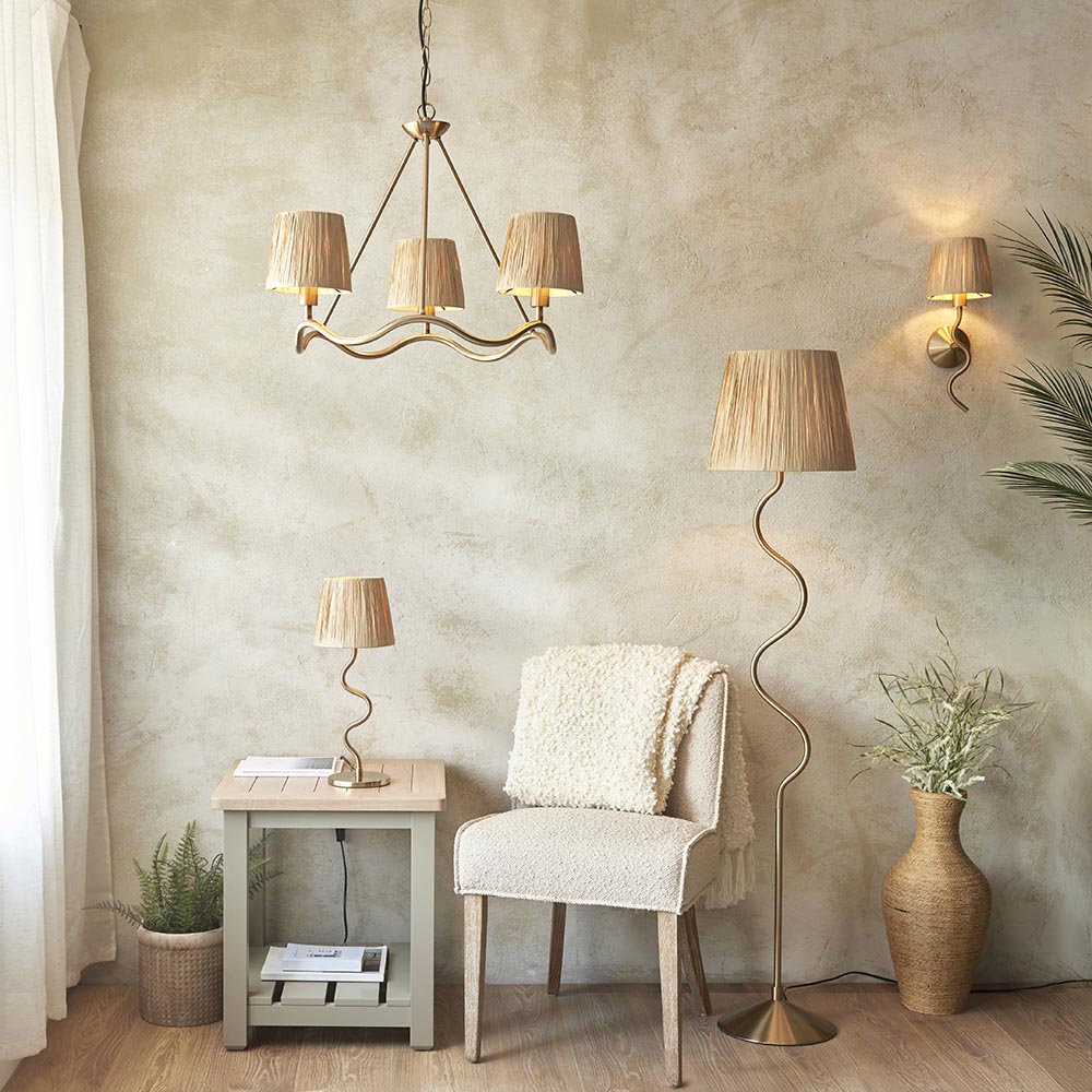 Danemont 3 Light Floor Lamp in aged brass with wriggle stem and tapered raffia shades, shown in a living room beside a chair and side table.