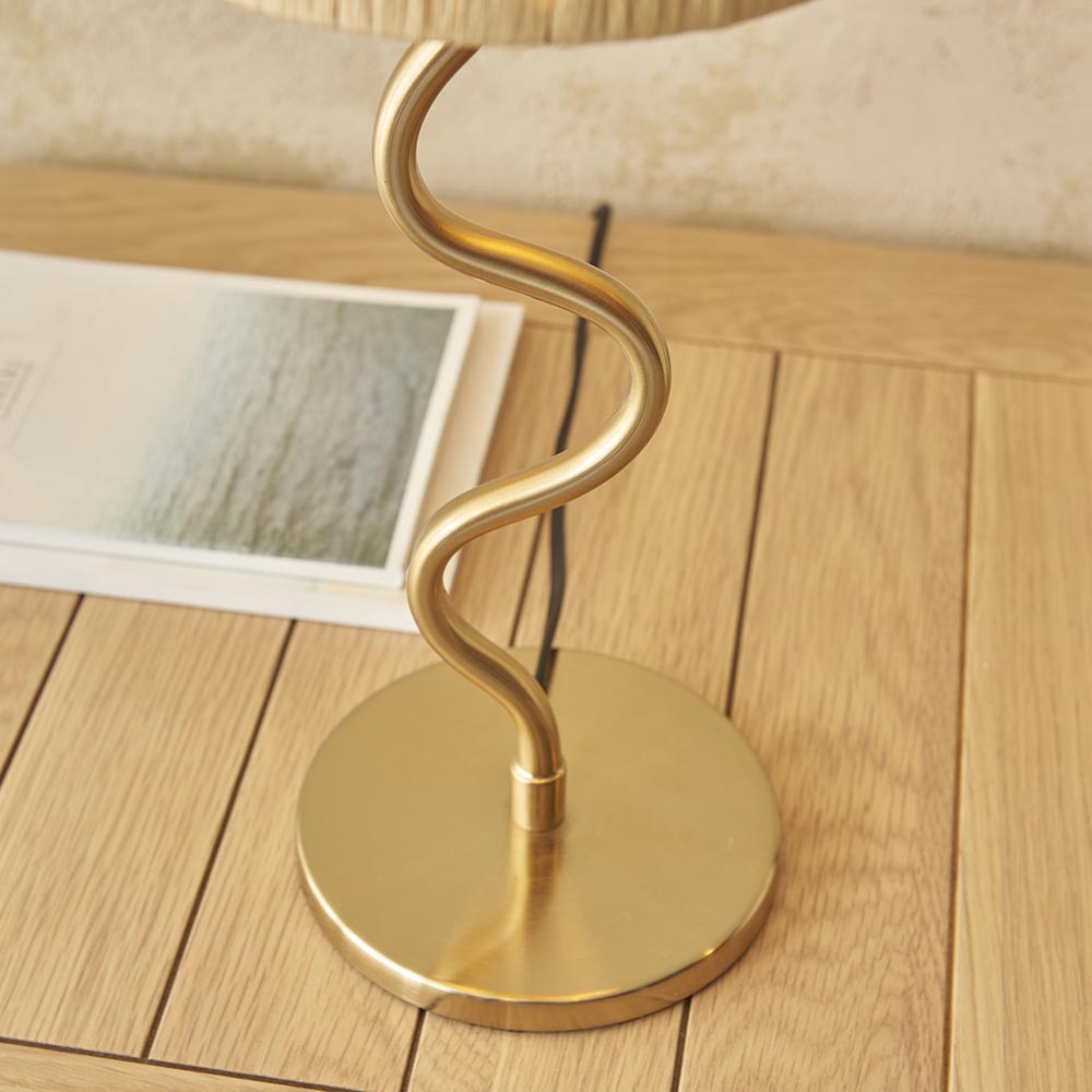 Endon Danemont table lamp close-up showing the brushed brass wavy stem and round base on a wooden floor beside a magazine.