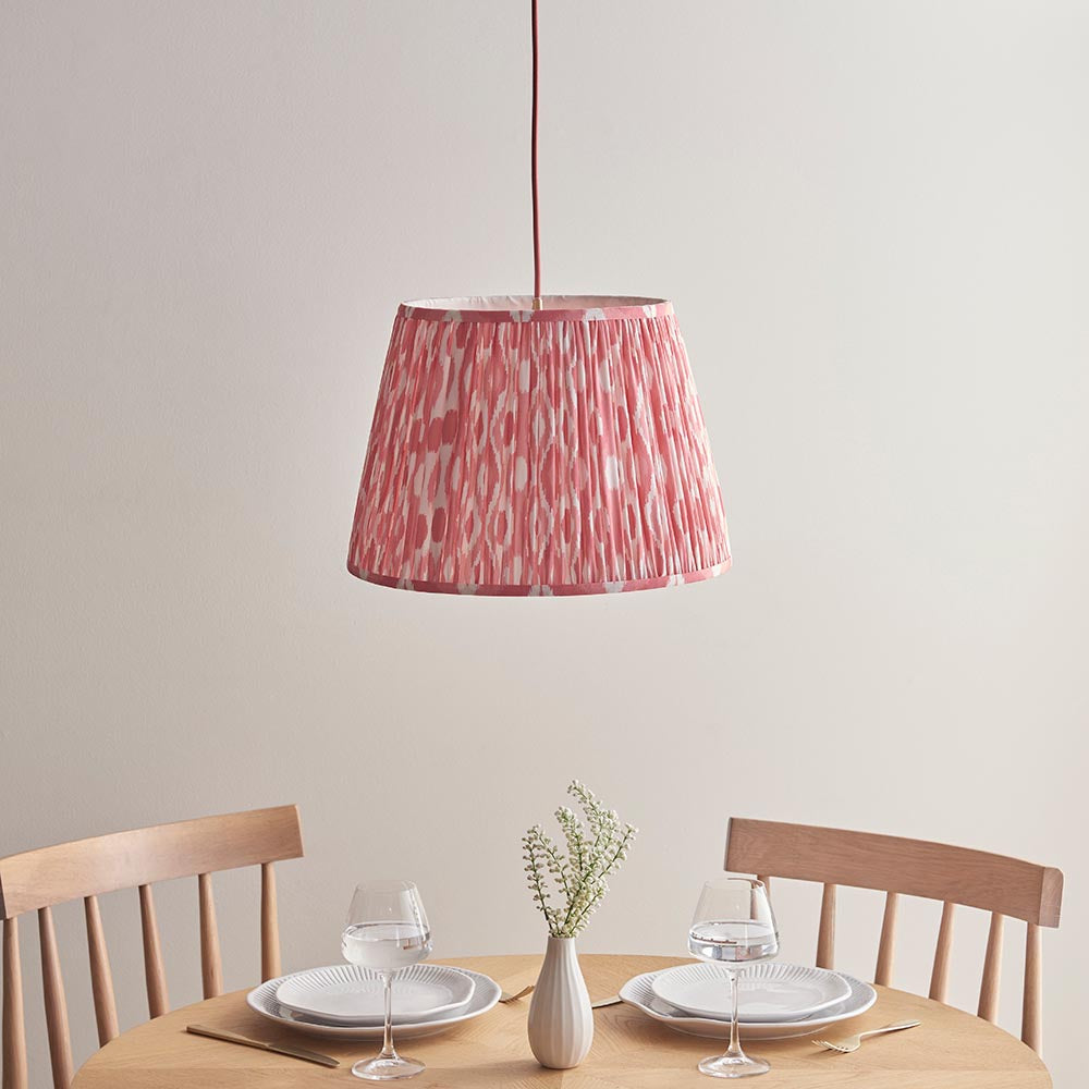 Endon Brackmont Ikat Coral pendant with handmade pleated faux silk shade in pink print and red braided cable, hanging above a wooden dining table.