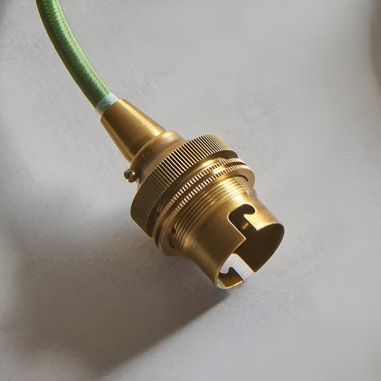 Brackmont Pendant close-up showing the brass B22 lampholder with ridged detailing and green fabric flex, set against a plain light background.