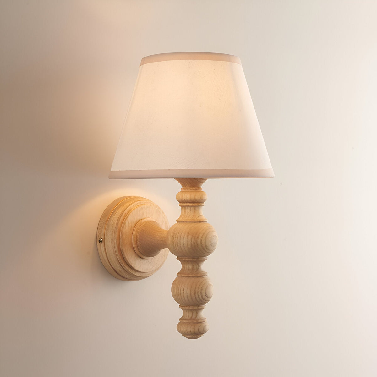 Aldworth Ivy Wall Light in natural turned ash wood with a tapered ivory fabric shade and round wall mount, shown on a plain light background.