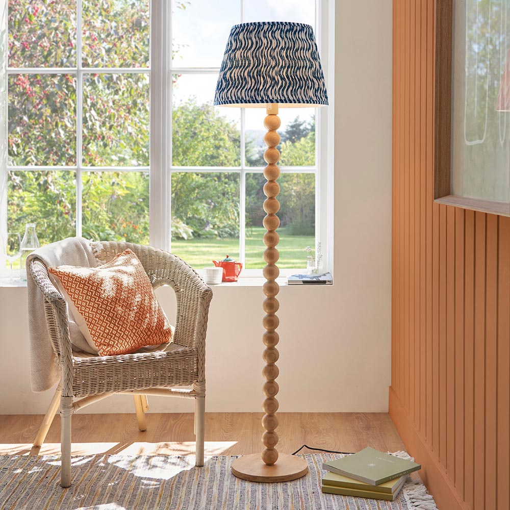 Endon Ashwood floor lamp with stacked bamboo sphere base and blue printed tapered shade, beside a wicker chair by a sunlit window.