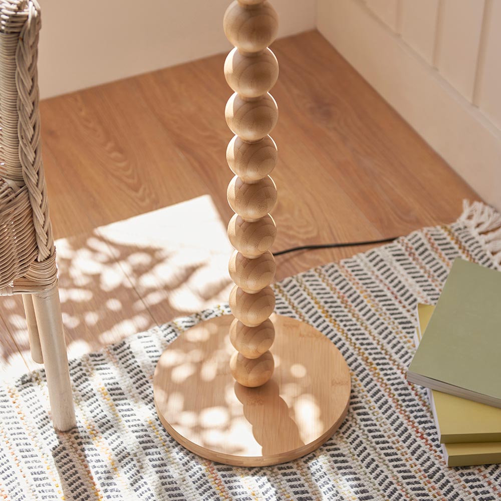 Endon Ashwood floor lamp base with stacked natural bamboo spheres on a round wooden plinth, set on a woven rug beside a rattan chair.