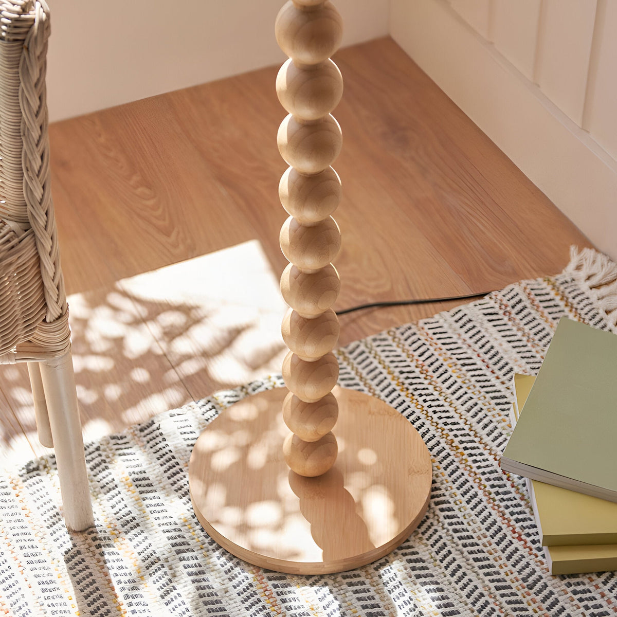 Ashwood Zigzag Floor Lamp base close-up, showing stacked bamboo spheres on a round wooden foot beside a woven rug and wicker chair.