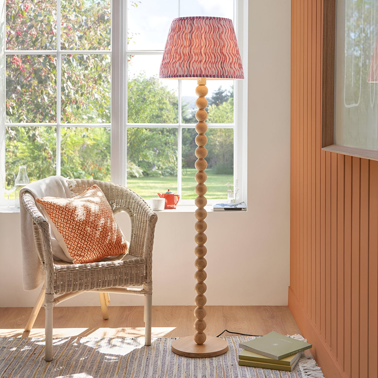Endon Ashwood floor lamp with stacked bamboo sphere base and pink Ripple pleated tapered shade, beside a wicker chair by a sunlit garden window.