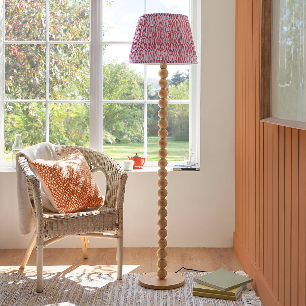 Endon Ashwood floor lamp with stacked bamboo sphere base and pink Ripple pleated shade, beside a rattan chair in a sunlit living room.