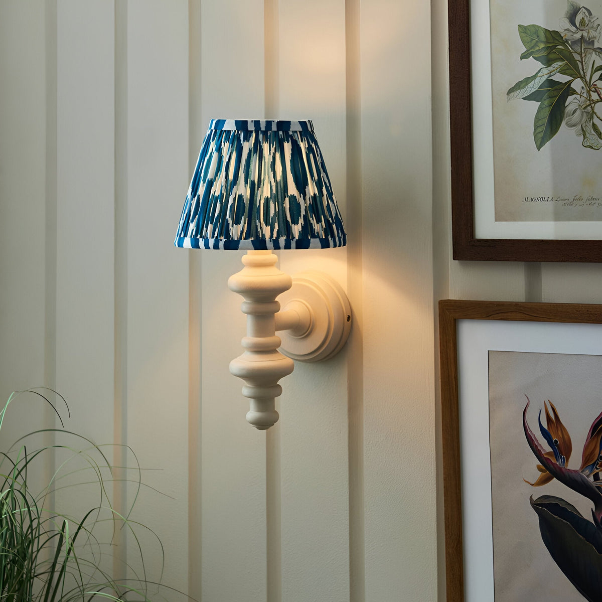 Bevbury Ikat wall light with turned white spindle base and blue and white patterned tapered shade, mounted on a panelled wall beside framed botanical prints.
