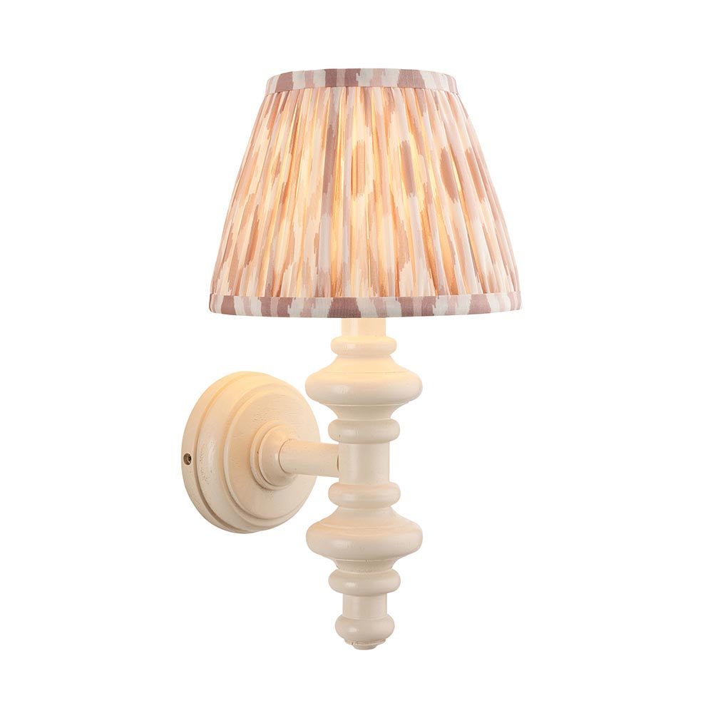 Endon Bevbury Ikat wall light with a white turned wooden spindle, brass B22 lamp holder and tapered pleated Ikat shade in pink and natural tones.