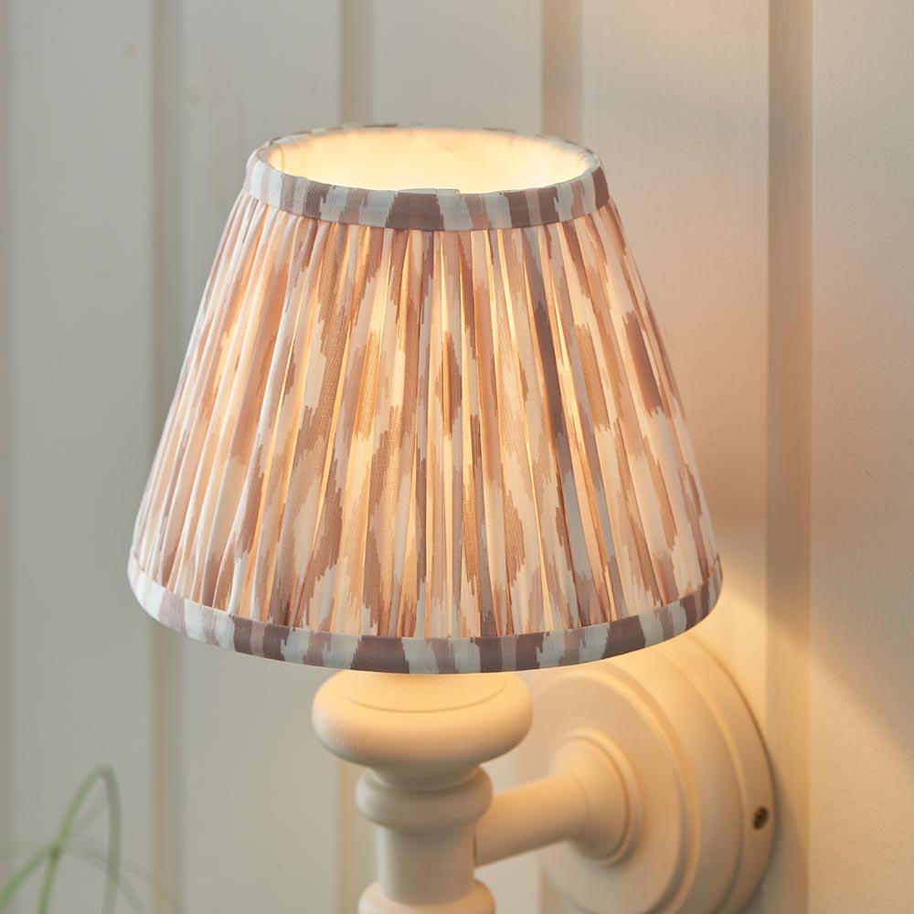 Endon Bevbury Ikat wall light with white turned spindle base and tapered pleated ikat fabric shade in natural and grey tones, illuminated on a panelled wall.