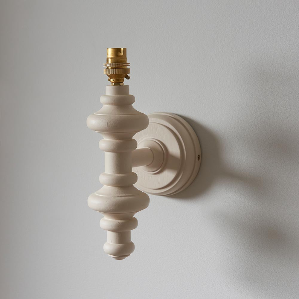 Endon Bevbury Ikat wall light base in satin white with turned wooden spindle and brass B22 lamp holder, mounted on a plain light wall without its shade.