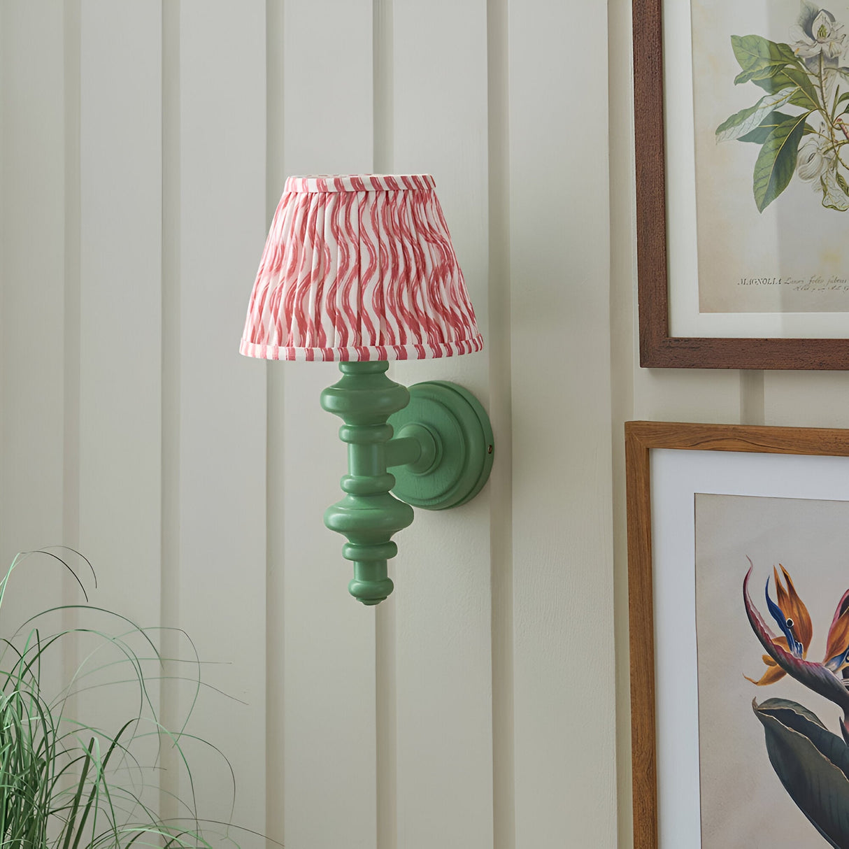 Endon Bevbury Ripple wall light with green turned wood spindle and pink rippled pleated shade, mounted on panelled wall beside framed botanical prints.