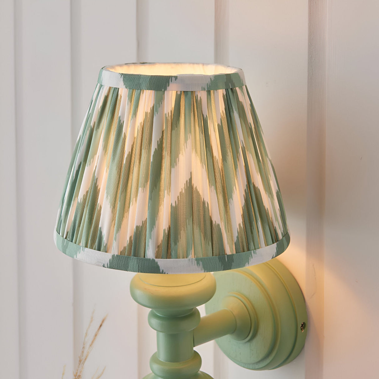 Endon Bevbury Zigzag wall light with a green turned wooden spindle, brass B22 lamp holder, and tapered pleated shade in green and cream zigzag print.