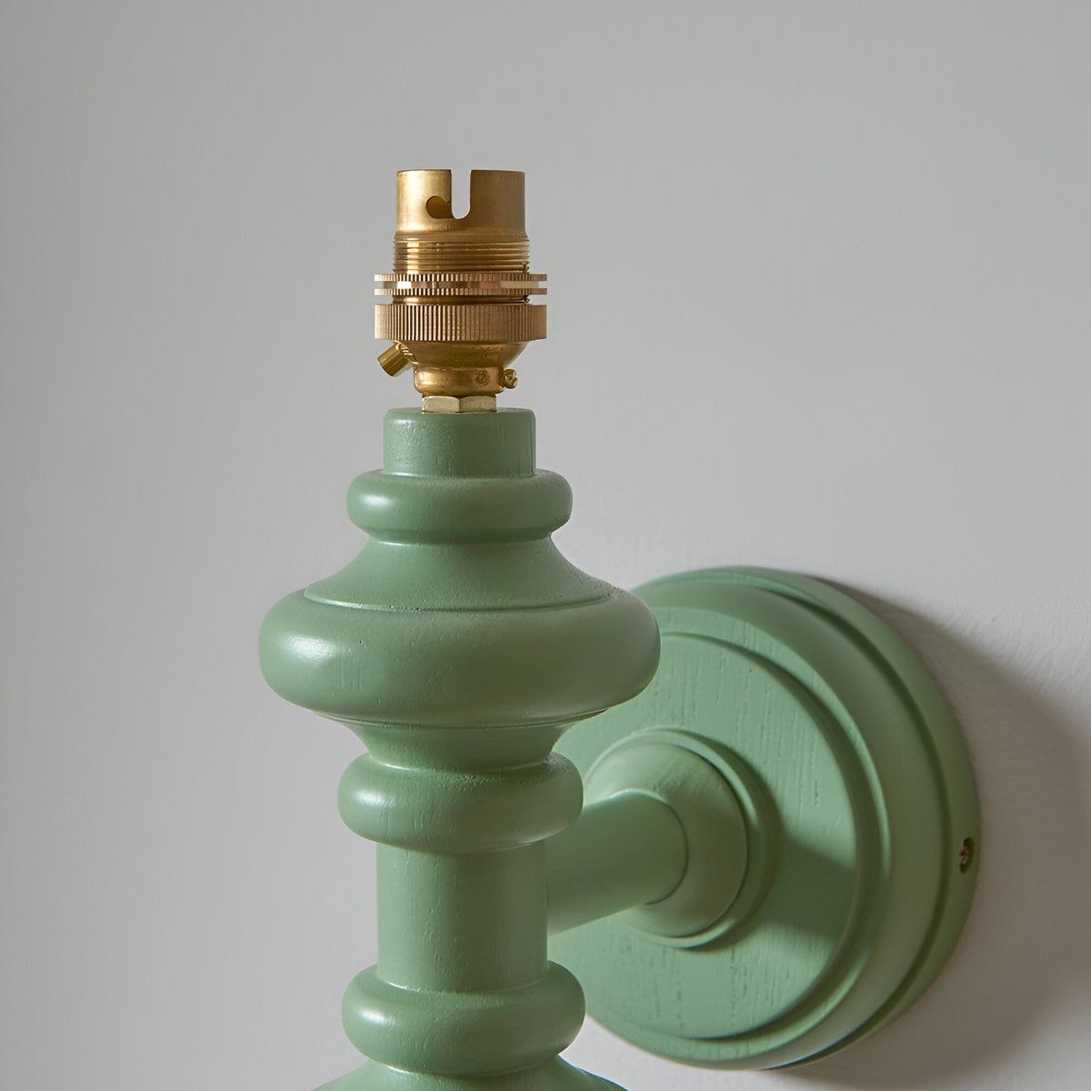 Close-up of the Endon Bevbury Zigzag wall light showing the green satin-painted turned wood spindle, brass B22 lamp holder and round wall plate.