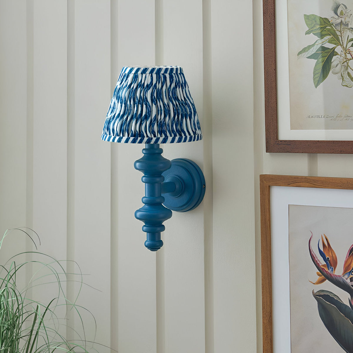Endon Bevbury Ripple wall light with blue turned wooden spindle and blue and white rippled faux linen shade, mounted on panelled wall beside botanical prints.
