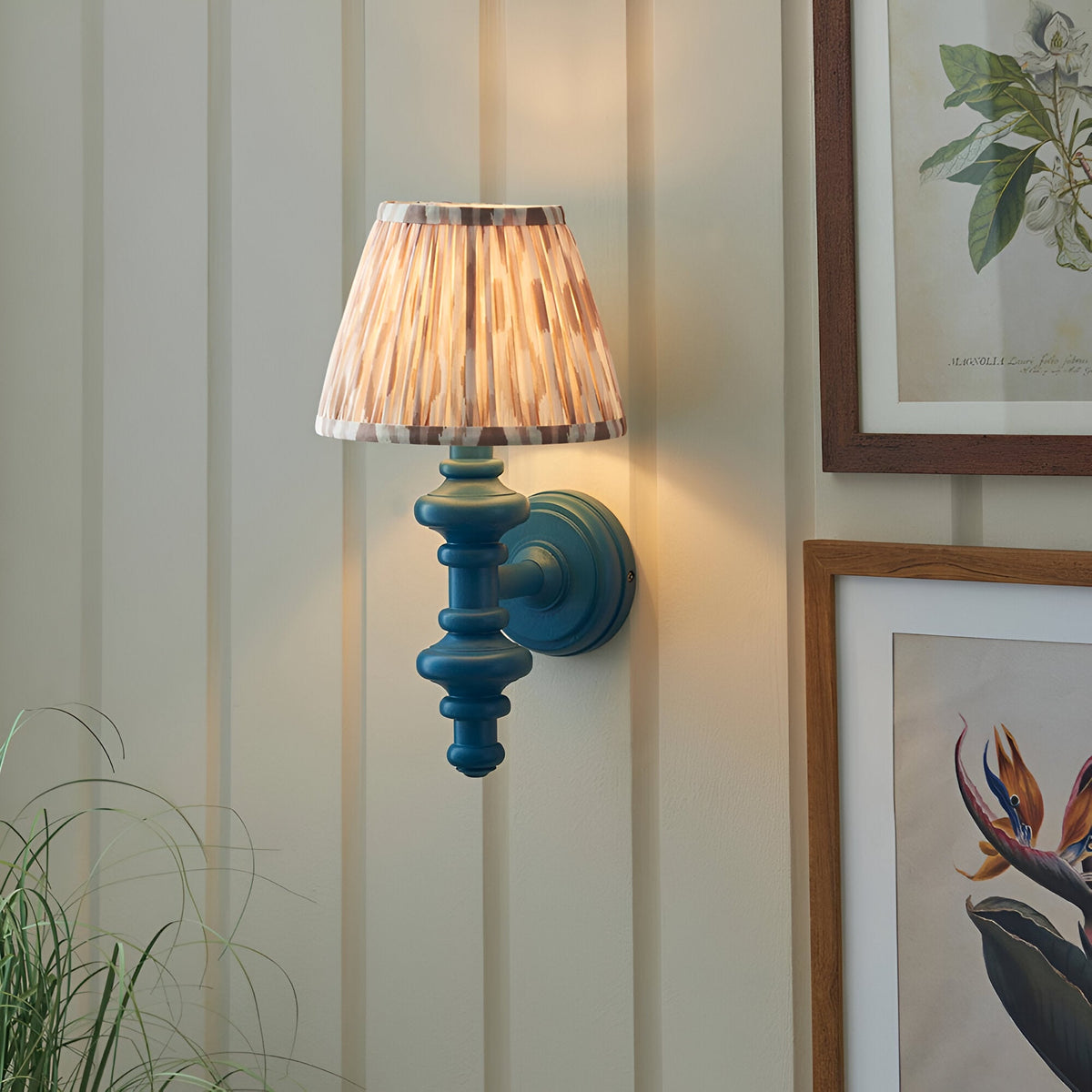 Endon Bevbury Ikat wall light with blue turned wood spindle and tapered pleated ikat shade, mounted on panelled wall beside botanical prints.