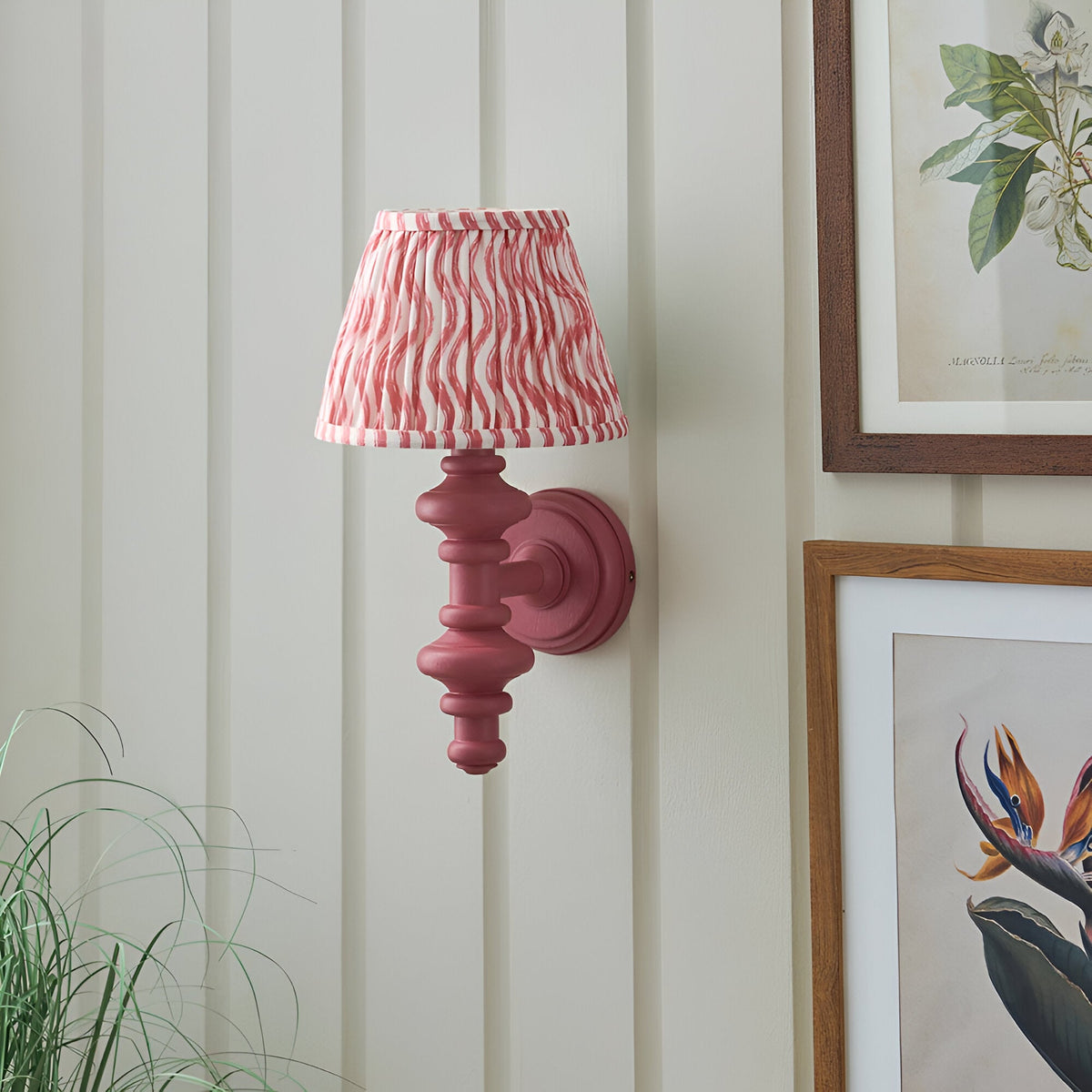 Endon Bevbury Ripple wall light with pink turned wood spindle and pleated pink ripple-print shade, mounted on panelled wall beside framed botanical prints.