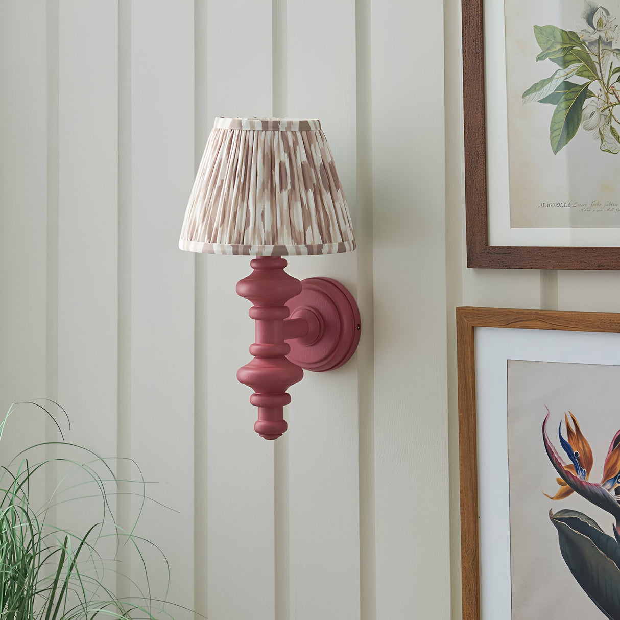 Bevbury Ikat wall light with pink-toned turned wooden spindle base and pleated Ikat-print fabric shade, mounted on a panelled wall near framed botanical prints.