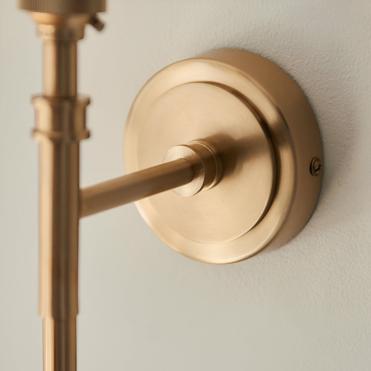 Close-up of the Bevford Leaf Wall Light's brass wall mount and arm, showing the round backplate, screw fixing, and knurled detailing against a plain light wall.